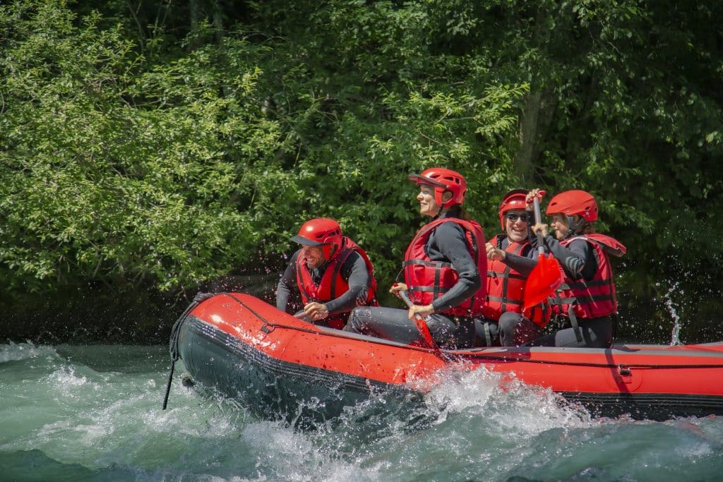 quatre personnes avec des gilets rouges et casque rouge entrain de faire du rafting