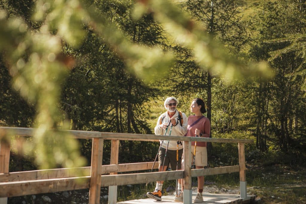 un homme et une femme en tenue de randonnée marchent dans la foret sur un pont en bois